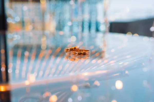 Goldene Eheringe liegen in Großaufnahme auf einem Glastisch — Stockfoto