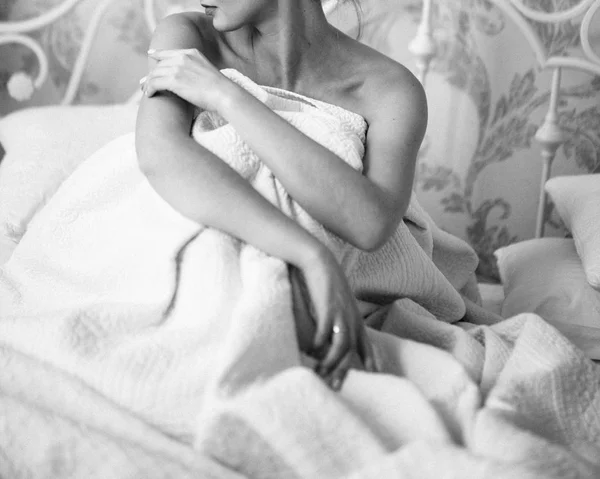 Mladá žena sedí ráno v posteli a kryje se s bílou přikrývkou. — Stock fotografie