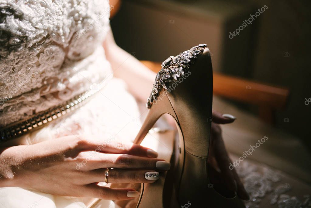 Bride in a white wedding dress holding wedding shoes in her hands
