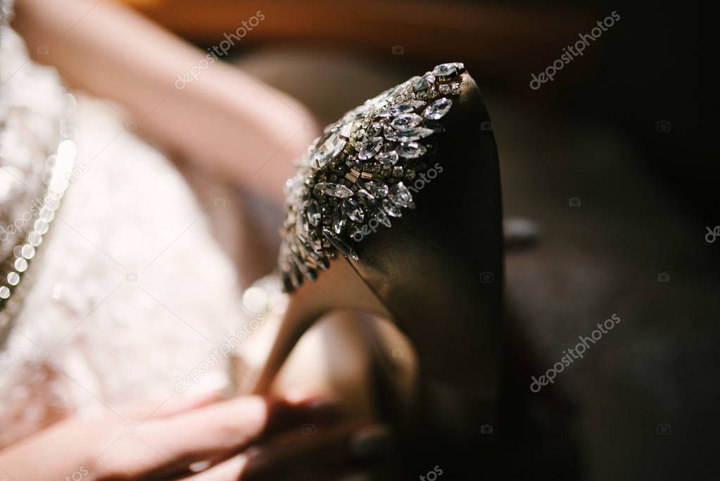 Bride in a white wedding dress holding wedding shoes in her hands