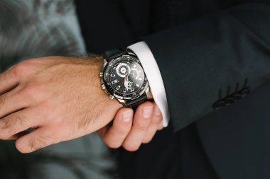 Takım elbiseli bir adam elindeki saati yakın alerler..