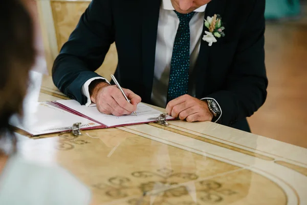 A vőlegény az esküvőn helyezi az aláírást a dokumentum. — Stock Fotó