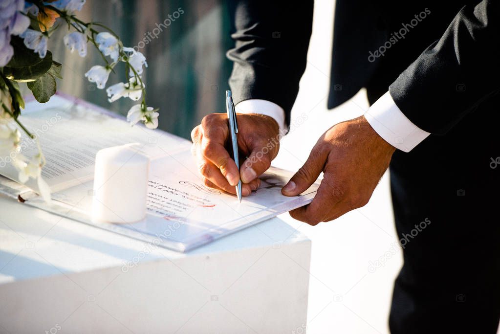 The groom at the wedding ceremony puts his signature on the document.