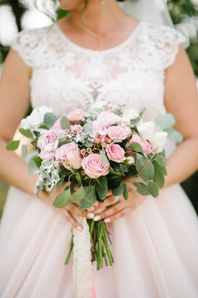 Mariée dans une robe de mariée tenant un bouquet de mariage dans ses mains gros plan — Photo