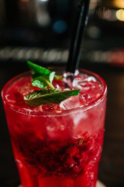 Buzlu, çilekli, samanlı ve nane yapraklı bir bardakta kırmızı bir içecek.