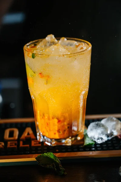 A orange drink in a glass with ice cubes, orange,straw and mint leaves