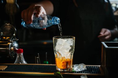 El barmeni kokteyl yapar. Kokteylde portakal ve nane yaprakları var..