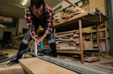 Marangozluk atölyesinde çalışma süreci. Tulumlu bir adam marangozluk atölyesinde çalışır. Bir adam dairesel testere üzerinde çalışır.