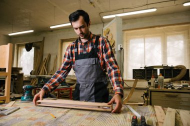 Marangozluk atölyesinde çalışma süreci. Tulumlu bir adam marangozluk atölyesinde çalışır. Meslek, marangozluk, marangozluk ve insan konsepti.