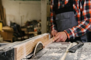 Marangozluk atölyesinde çalışma süreci. Marangozluk atölyesinde çalışan bir adam. Marangoz, kereste fabrikasında tahta kesmek için testere makinesi kullanıyor. Meslek, marangozluk, marangozluk, marangozluk.