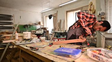 Marangozluk atölyesinde çalışma süreci. Tulumlu bir adam marangozluk atölyesinde çalışır. Meslek, marangozluk, marangozluk ve insan konsepti.