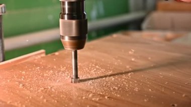 Marangozluk atölyesinde çalışma süreci. Marangozluk atölyesinde çalışan bir adam marangozluk atölyesinde çalışıyor. Bir adam sondaj makinesiyle ahşap tahta deliyor. Meslek, marangozluk, marangozluk ve insan konsepti.