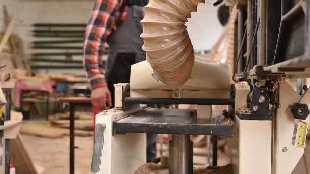 Proceso de trabajo en el taller de carpintería.Un hombre en overoles utiliza una máquina cepilladora de engrosamiento en un taller de carpintería.Profesión, carpintería, carpintería y concepto de personas — Vídeos de Stock