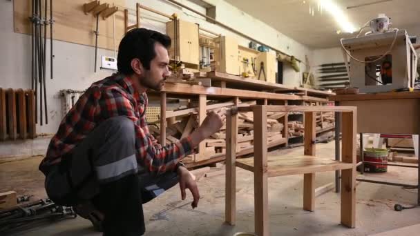 木工職人は 木のテーブルにニスを置きます 労働者は家具を生産する工場で木の詳細を塗装しています ブラシ付きの男の手は乾燥油を適用しています — ストック動画