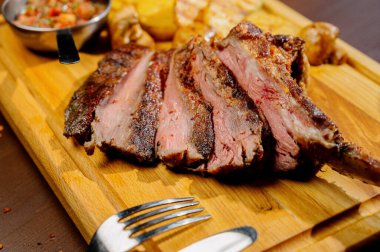 Tabakta et ve kızarmış patatesle ahşap bir masada yemek.