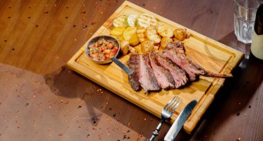 Tabakta et ve kızarmış patatesle ahşap bir masada yemek.