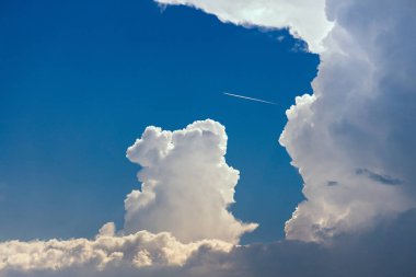 Mavi gökyüzünde renkli, büyük ve kabarık Cumulonimbus fırtına bulutlar. Güzel güneş ışığı ve gökyüzünde bir uçak