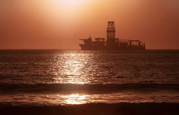 A large vessel on horizon in the atlantic ocean under the bright sun and red sunset.  Sunlight reflection off the water