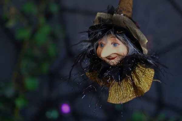 Halloween holiday background. A figurine of flying aged witch with kindness face on a dark blurred background of cobwebs. Concept of all hallows eve.