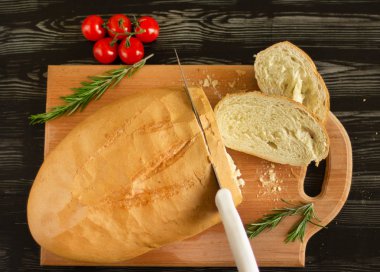 Beyaz ekmek ahşap bir tahtanın üzerinde bıçakla dilimlenir kiraz domatesleri ve biberiyeyle.