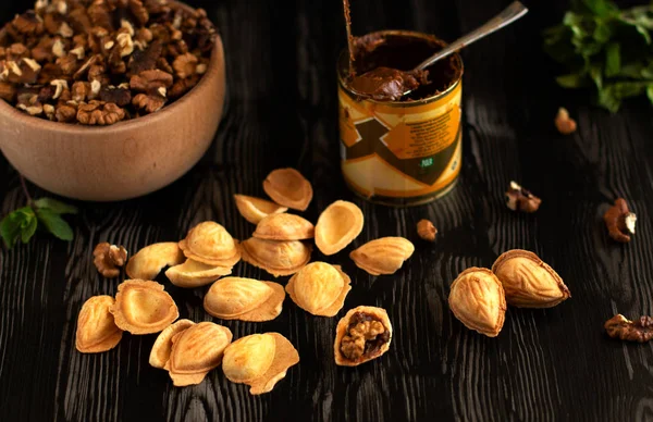 Cookies in the form of nuts with condensed milk and nuts on a dark wooden table with greens