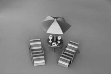 İki bardak ve masada bir tatlı ile bir güneş şemsiyesi altında iki şezlong, plajda yeşil yaprakları altında. Bir şezlong, yaslanmış, şezlong bir palmiye ağacı altında Yaz tatili.