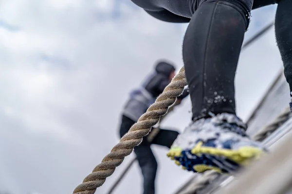 A man overcomes an obstacle at a sporting event. Cloudy weather. Sneakers and rope