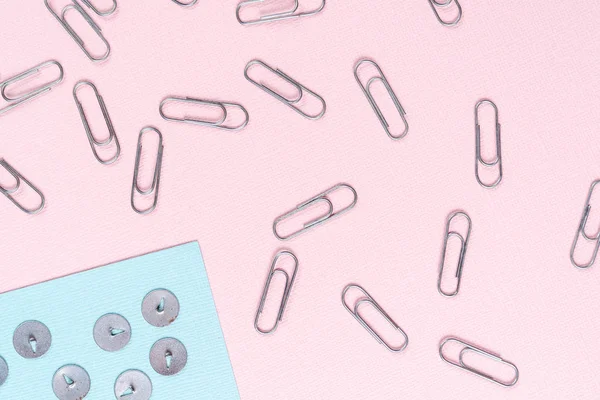 Metal push pins and paper clips scattered on blue and pink sheets of paper