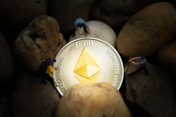 Miniature miners digging golden Ethereum coin (ETH) in mine