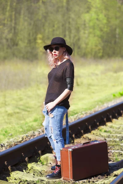 Beautiful traveling woman with a suitcase on the railroad tracks