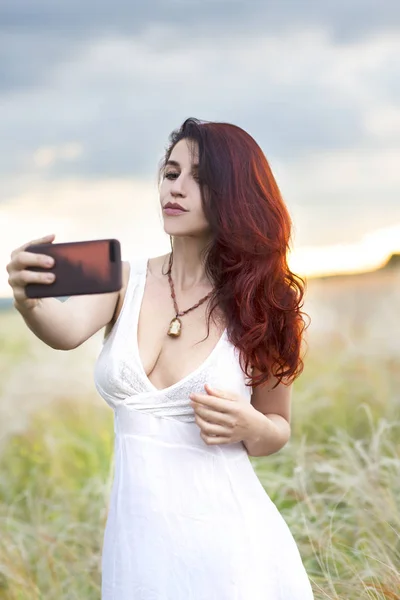 beautiful woman with a mobile phone in nature makes photo of herself