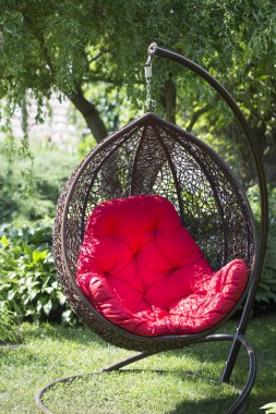 Bahçede asılı kırmızı yastıklı hasır sallanan sandalye.