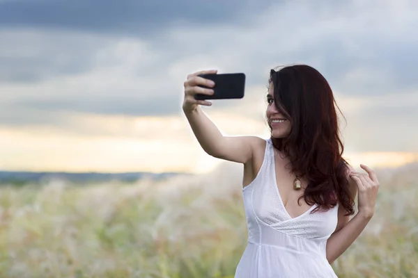 beautiful woman with a mobile phone in nature takes a photo of herself against the backdrop of the sunset