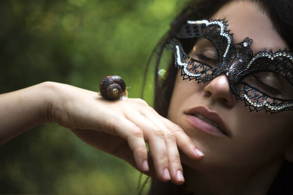 красивая женщина в венецианской маске держит улитку на руке
