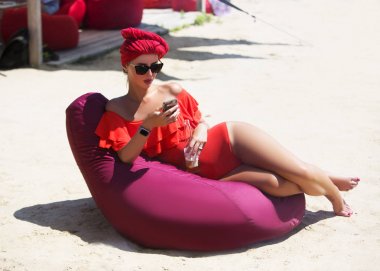Şişe ve akıllı telefon içki ile plajda tabaklanmış seksi genç kadın