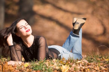 Parktaki sarı yaprakların üzerinde yatan güzel bir kadın. Sıcak bir sonbahar gününde boş zaman..
