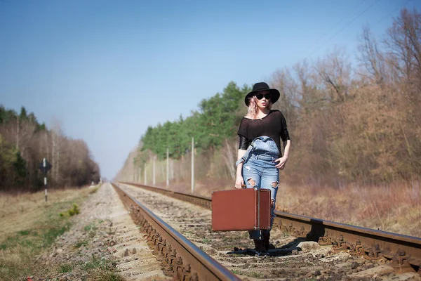Young beautiful traveling woman with a suitcase walks along the railway