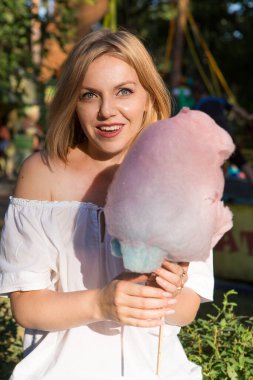 Gülen genç kadın lunaparkta pamuk şeker yiyor.