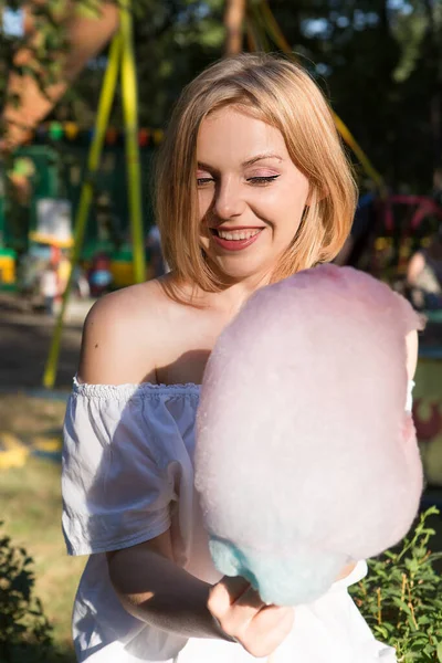 Lunaparkta pamuk şeker yiyen mutlu genç bir kadın.