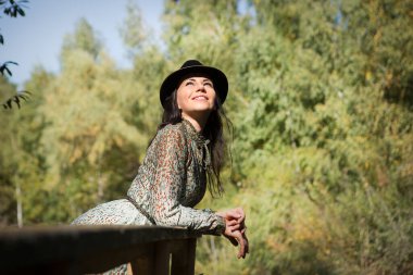 Güzel genç bir kadın gölün ve ormanın arka planında parkta dinleniyor..