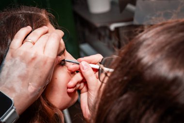 Makyaj sanatçısı, profesyonel bir kuaförde genç ve güzel bir kıza makyaj yapıyor. Güzellik, moda ve cilt bakımı endüstrisi. Makyaj sanatçısının işi. Göz kapaklarına gözkapağı uygulanıyor.