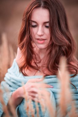 Gün batımında çimenli bir tarlada örgü örülü süvetere sarılmış genç ve seksi bir kadının portresi. Sonbahar aşkı.