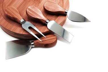 Beyaz arka planda izole edilmiş ahşap bir çekiş tahtasındaki çeşitli profesyonel peynir bıçakları. Boşluğu kopyala.