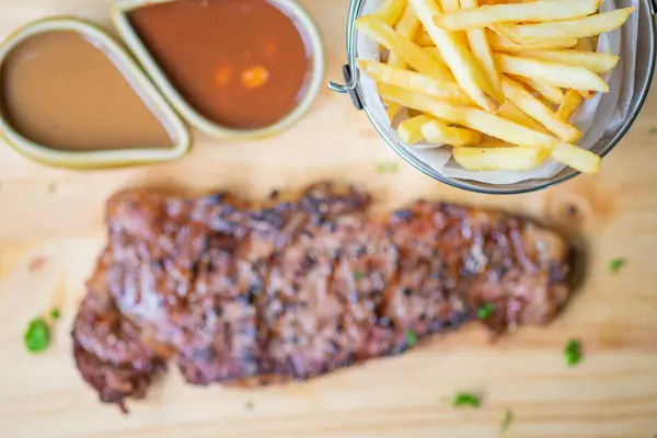 Bife com batatas fritas e molho em uma bandeja de madeira — Fotografia de Stock