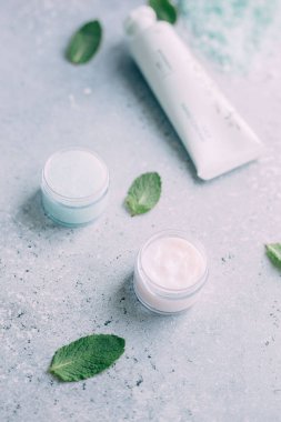Spa ve vücut bakımı ürünleri. Mavi fırçalama, beyaz krem yüz deniz tuzu, havlu, gri arka planda nane. Güzellik Cilt Bakımı. Spa tedavisi