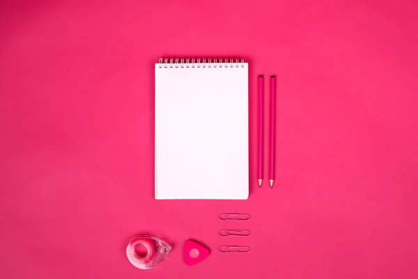 Pembe arka planda farklı okul malzemelerine sahip beyaz defter..