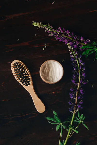 Hair mask. Hair brush. Purple flowers. Lavender. Dark wood background. Hair Products and Treatments