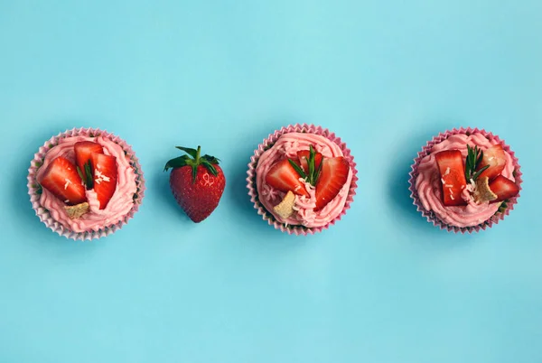 Layout of pink cakes with strawberries on a blue background, top view.
