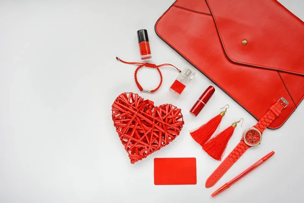 The layout of red objects: bag, lipstick, watches, earrings, nail polish, perfume, bracelet are on a white background side.