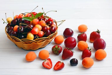 Kiraz ile çilek, erik, kiraz erik ve hasır sepet hafif ahşap bir masa üzerinde yalan, yakın çekim.